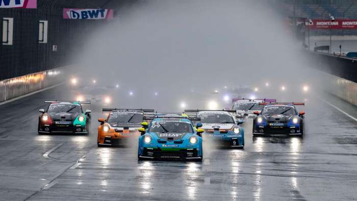 Image of a group of Porsche 911s racing on a wet racetrack throwing spray high into the air.