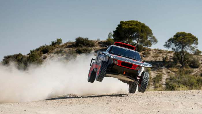 Image of the Audi RS Q e-tron E2 in the air after a jump with a large cloud of dust behind it.