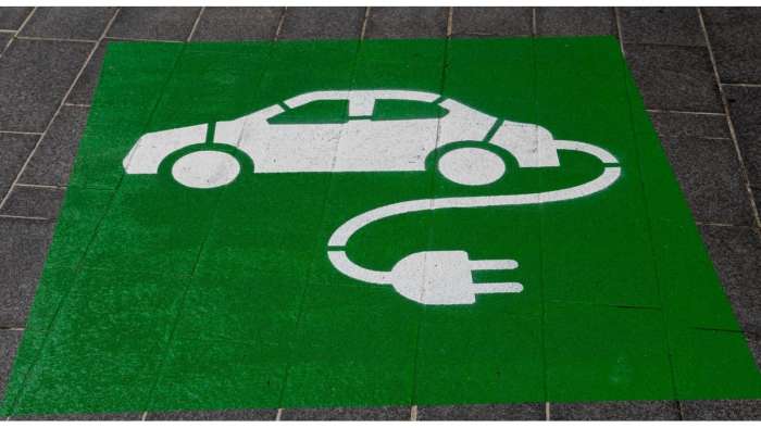 Parking area for EVs shows a white car with a power cord attached against a green background.