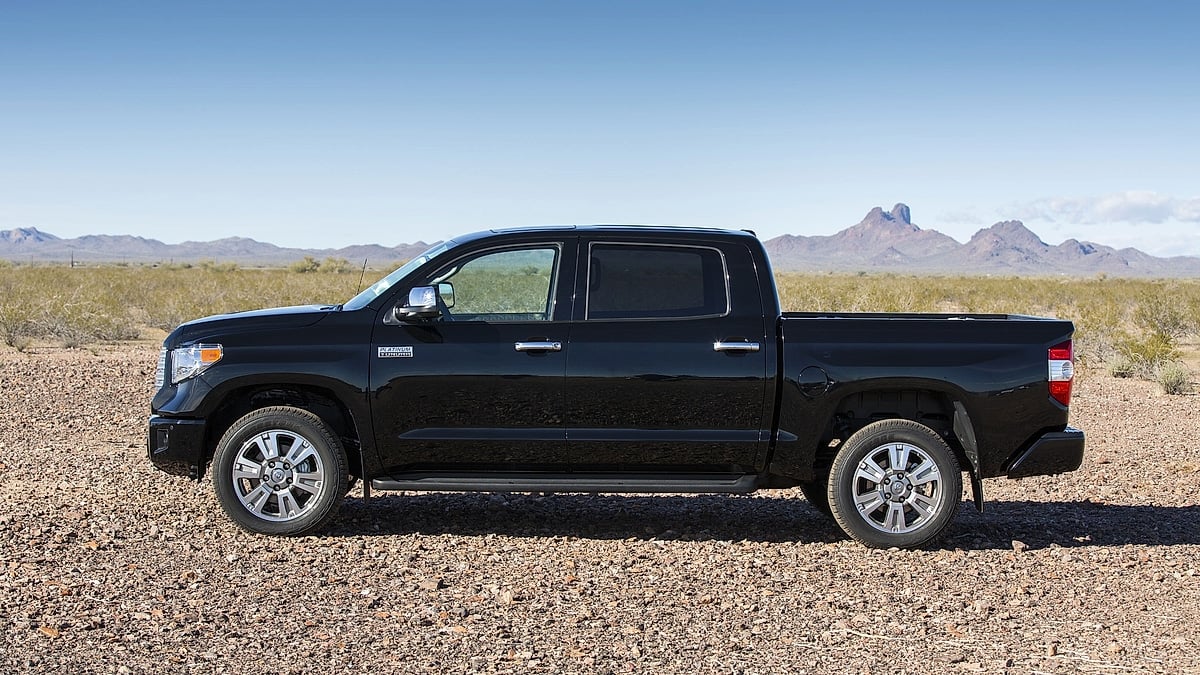 Black 2014 Toyota Tundra Platinum shown in side profile on rocky desert terrain with mountains in the background.