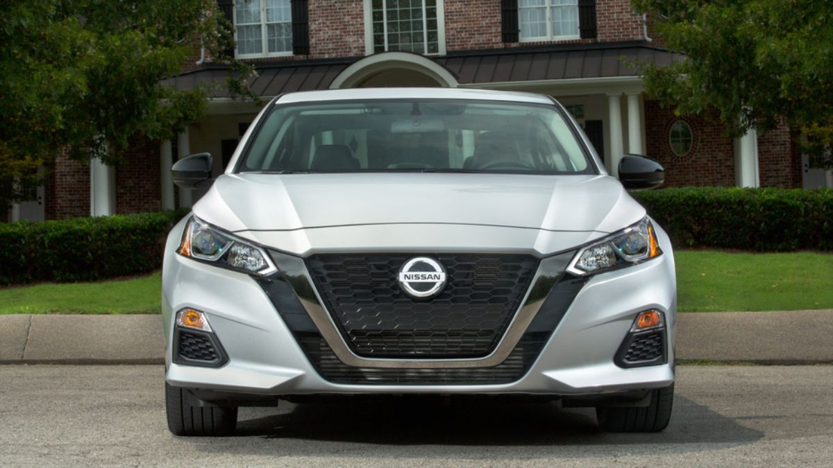 2019 Nissan Altima in silver, front-facing view with brick house and green lawn background
