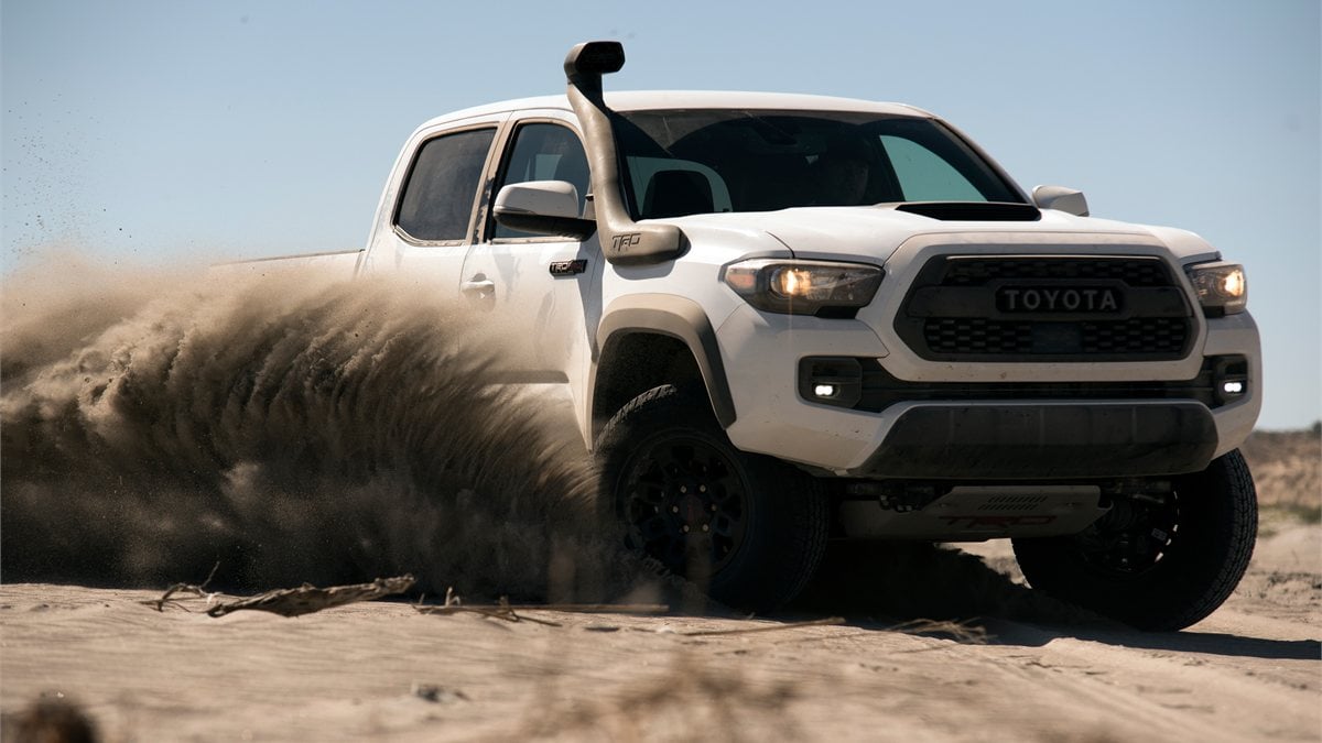 White Toyota Tacoma TRD Pro off-roading in sand, midsize pickup truck in action
