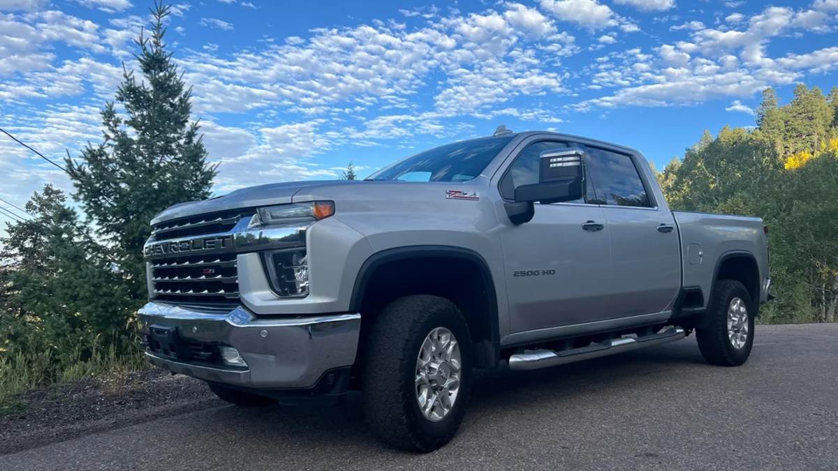 2022 Chevrolet Silverado 2500HD in silver, front three-quarter view, featuring chrome grille, tow mirrors, and lifted suspension against scenic mountain backdrop.