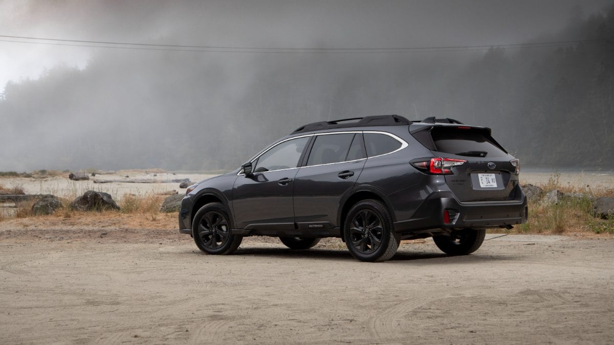 A dark gray/black 2021 Subaru Outback Onyx Edition photographed from the rear three-quarter angle, featuring black wheels and trim, parked on a dirt road against a moody, cloudy sky backdrop.
