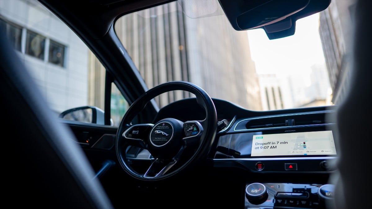 2021 Jaguar i-Pace interior view from driver's seat, sleek black dashboard with touchscreen showing dropoff time, modern urban setting