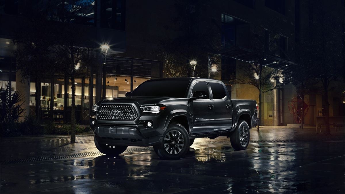 Black Toyota Tacoma pickup photographed at night on wet pavement in an urban setting, highlighting aggressive styling and premium trim.