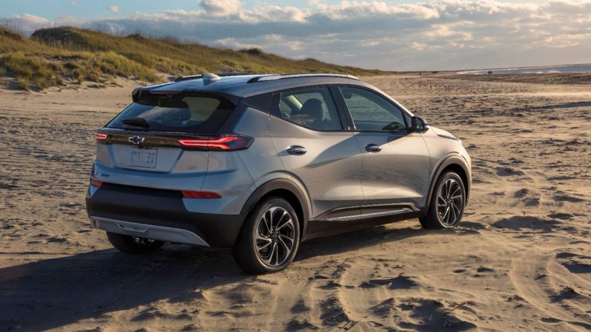 A silver Chevrolet Bolt EV parked on a sandy beach, with dune grass and a cloudy sky in the background.