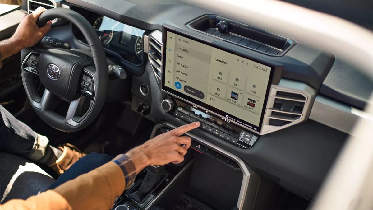 A person uses the infotainment touchscreen of a 2022 Toyota Tundra. The dashboard displays radio options with a modern, sleek design.