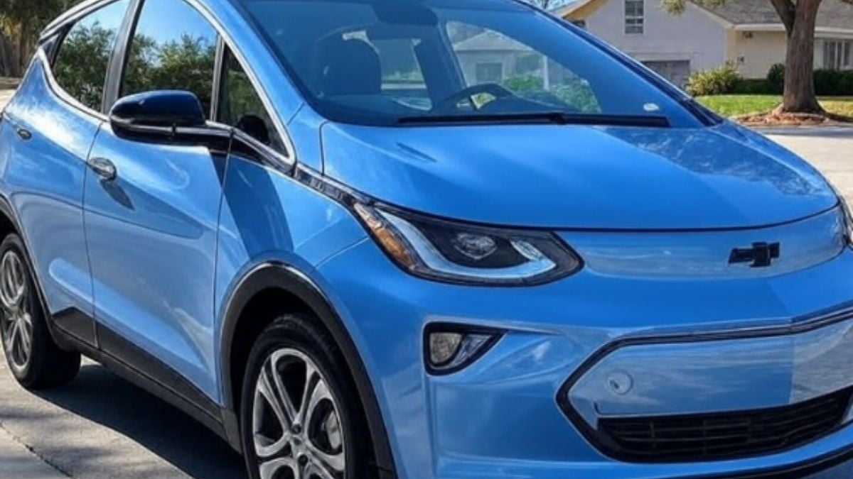 A Blue 2023 Chevrolet Bolt EUV is parked in a sunny suburban street, showcasing a sleek design with sharp headlights and shiny wheels, conveying modernity.