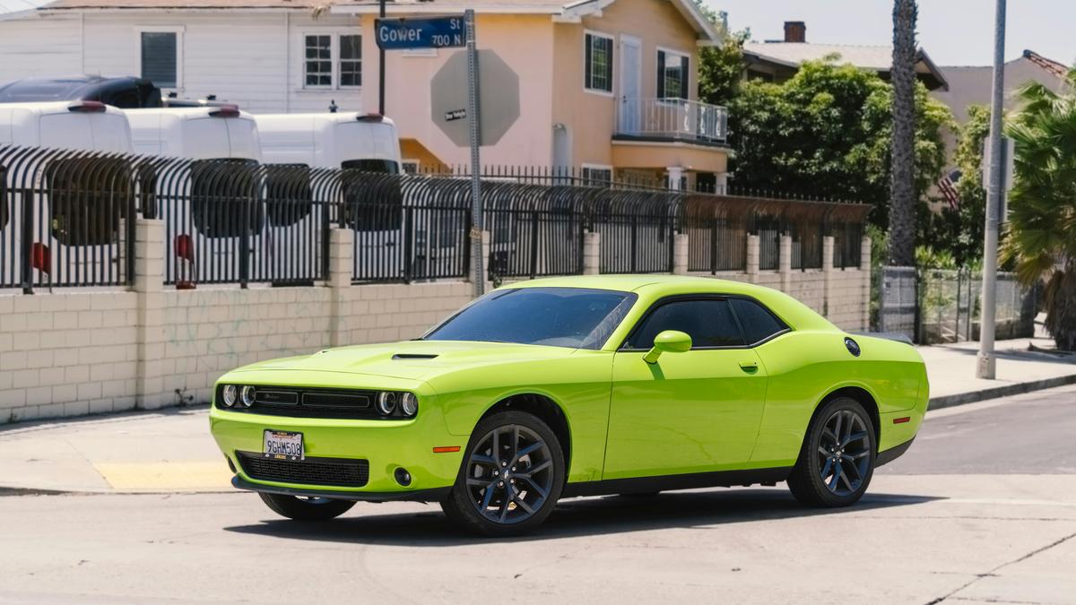 A vibrant lime-green Dodge Challenger parked on a city street, showcasing its sleek design and black alloy wheels.