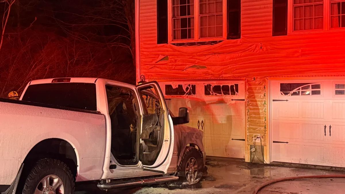 A white Ram truck parked in front of a garage with fire-damaged siding.