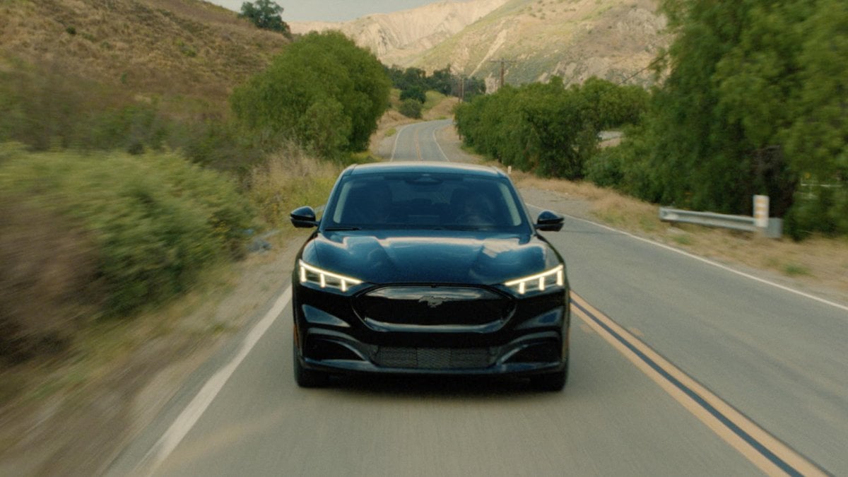 Black Ford Mustang Mach-E driving on winding mountain road with illuminated LED headlights