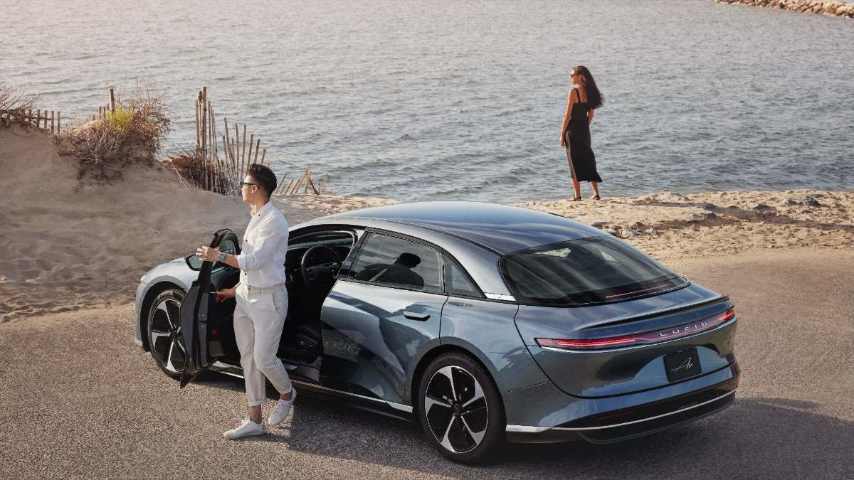 2023 Lucid Air Pure in metallic blue, parked on sandy beach with open door and stylish occupants