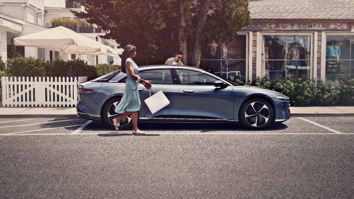 2023 Lucid Air Pure electric sedan side view in gray, two people entering vehicle in upscale neighborhood setting.