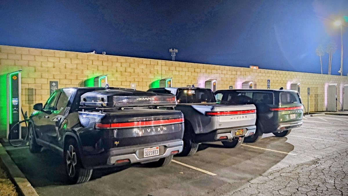 Rear three-quarter view of multiple Rivian R1T electric trucks parked at EV chargers at night.