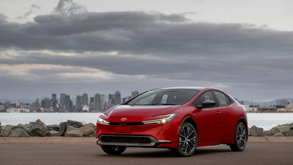 A red 2023 Toyota Prius parked with a city skyline and water in the background.