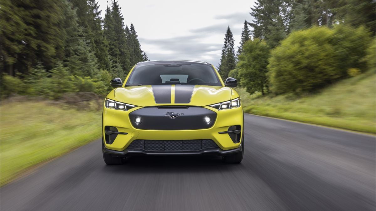 Front view of the 2023 Ford Mustang Mach-E Rally driving on a forest road, featuring rally-inspired styling, aggressive lighting, and all-electric performance.