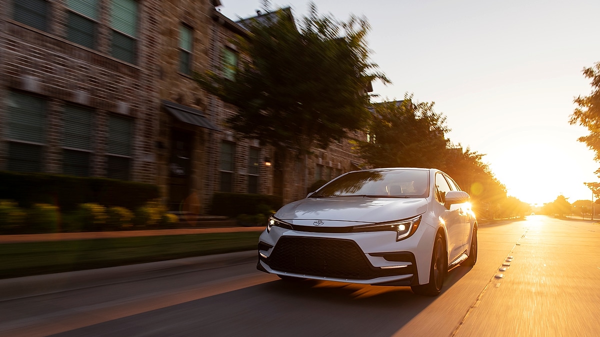 White 2023 Toyota Corolla XSE driving on a city street at sunset, shown from the front angle.