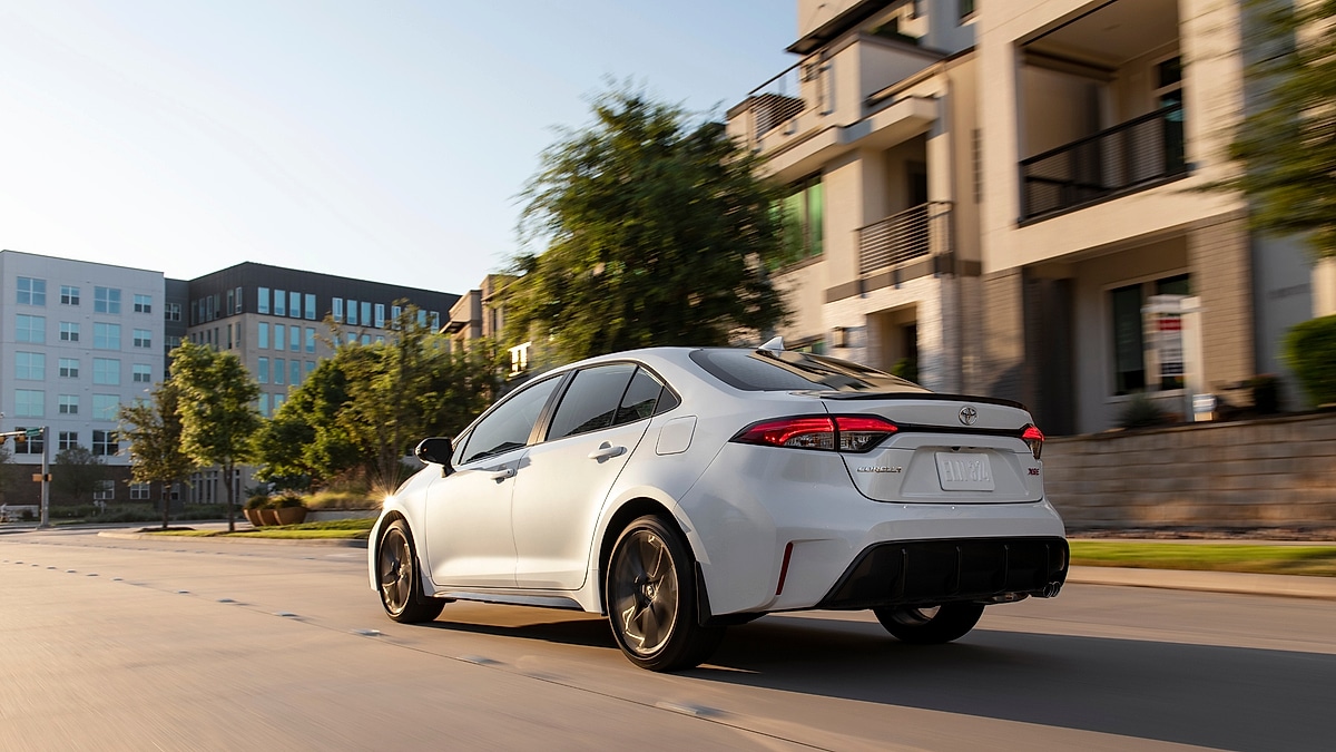 Rear three-quarter view of a white 2023 Toyota Corolla XSE driving on a city street.