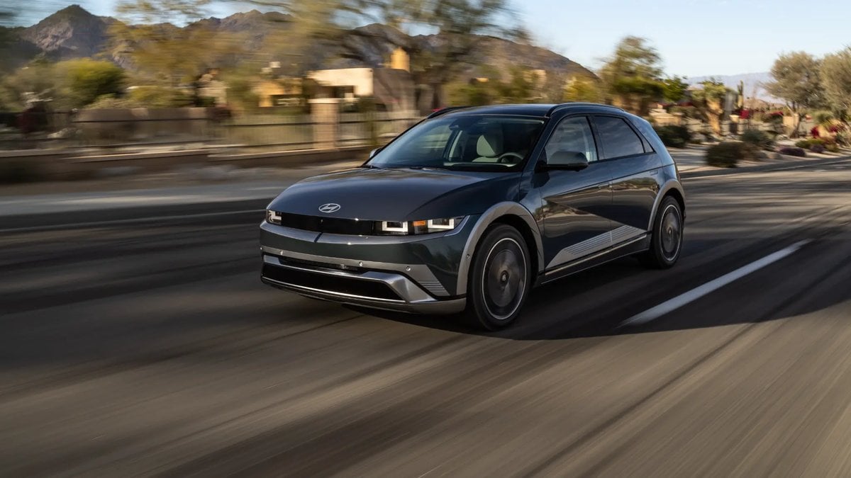 A black 2025 Hyundai Ioniq 5 electric crossover shown from the front three-quarter angle, driving on a desert road with mountains in the background during golden hour.