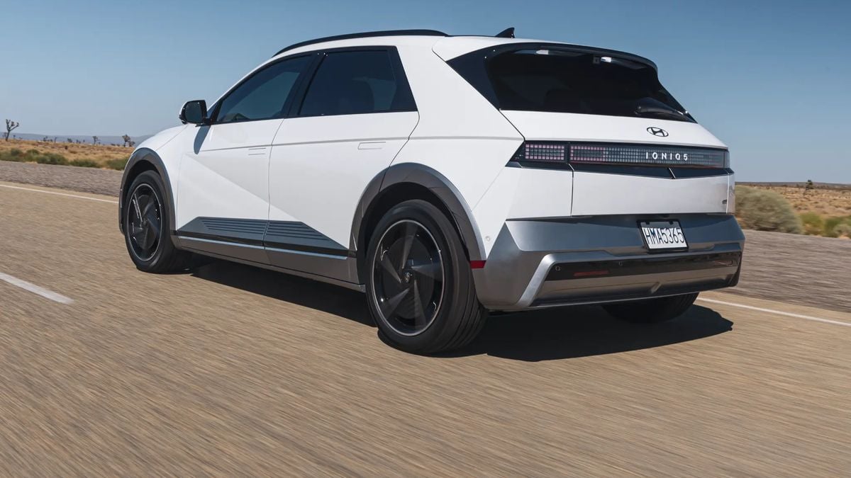 Rear three-quarter view of a white Hyundai Ioniq 5 electric SUV driving on a desert highway, showing pixel-style LED taillights, aerodynamic wheels, and modern EV design.