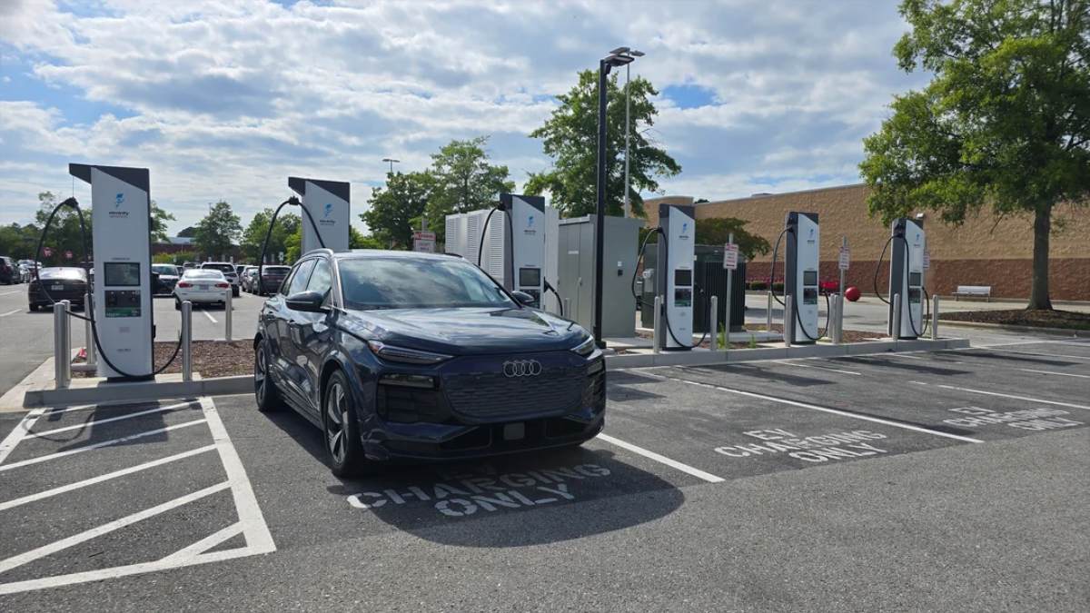 Dark blue 2024 Audi Q6 e-tron SUV charging at modern electric vehicle station with multiple white charging pillars