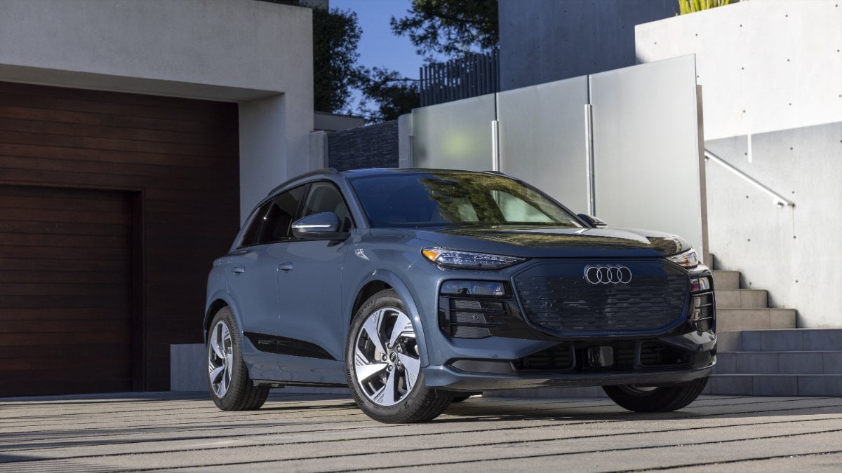 Slate blue 2024 Audi Q6 e-tron SUV parked on wooden deck, front angle view with modern architectural background