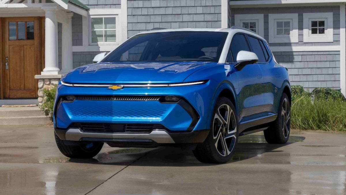 2024 Chevy Equinox EV in bright blue with a contrasting white roof parked in front of a house, displaying its clean electric SUV design and thin LED daytime running lights.