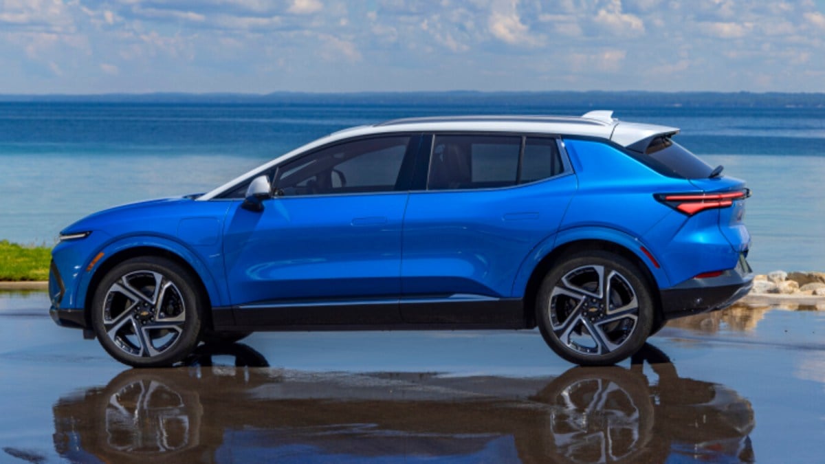 2024 Chevrolet Equinox EV in blue shown in side profile parked near a waterfront, highlighting aerodynamic SUV design and alloy wheels.
