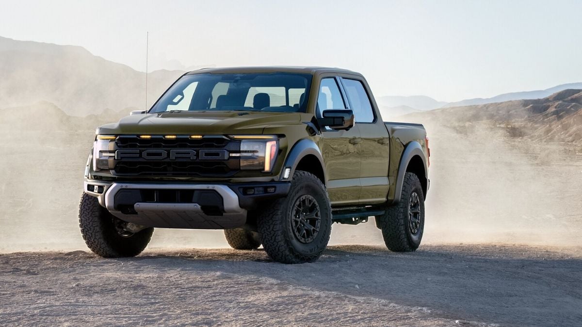 Green Ford F-150 Raptor driving off-road in a dusty desert landscape, with rugged tires and an aggressive front grille highlighted