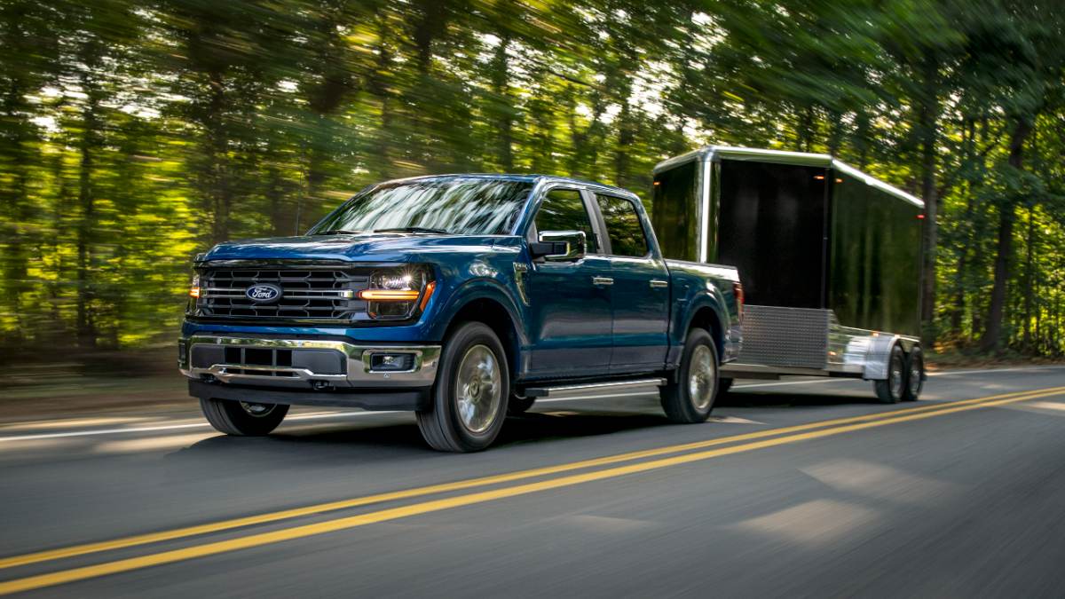2024 Ford F-150 XLT towing an enclosed trailer on a highway, front three-quarter view emphasizing towing performance.