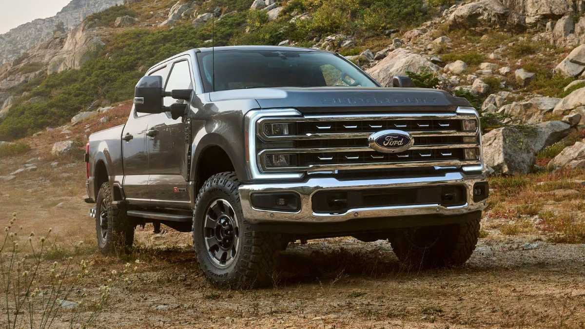 2023 Ford Super Duty F-250 in metallic gray, front three-quarter view, featuring chrome grille and off-road tires, photographed on rocky mountainous terrain.