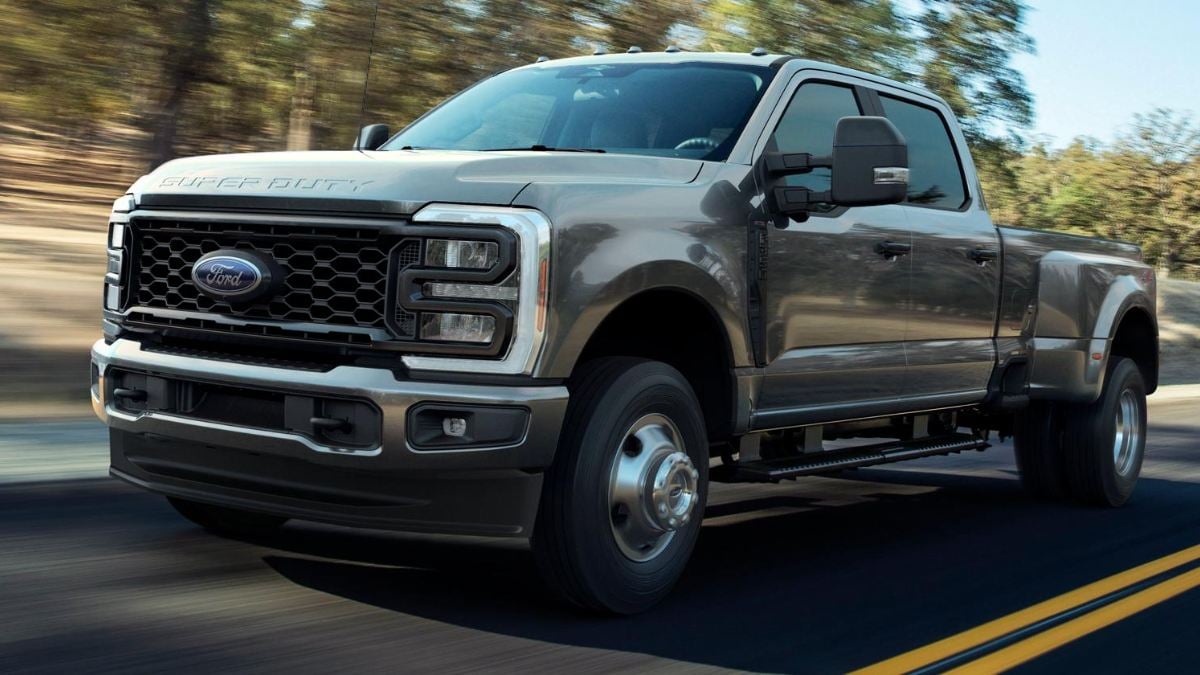 2023 Ford Super Duty F-250 in metallic gray, front three-quarter view, featuring bold honeycomb grille and LED headlights, photographed in motion on rural road.