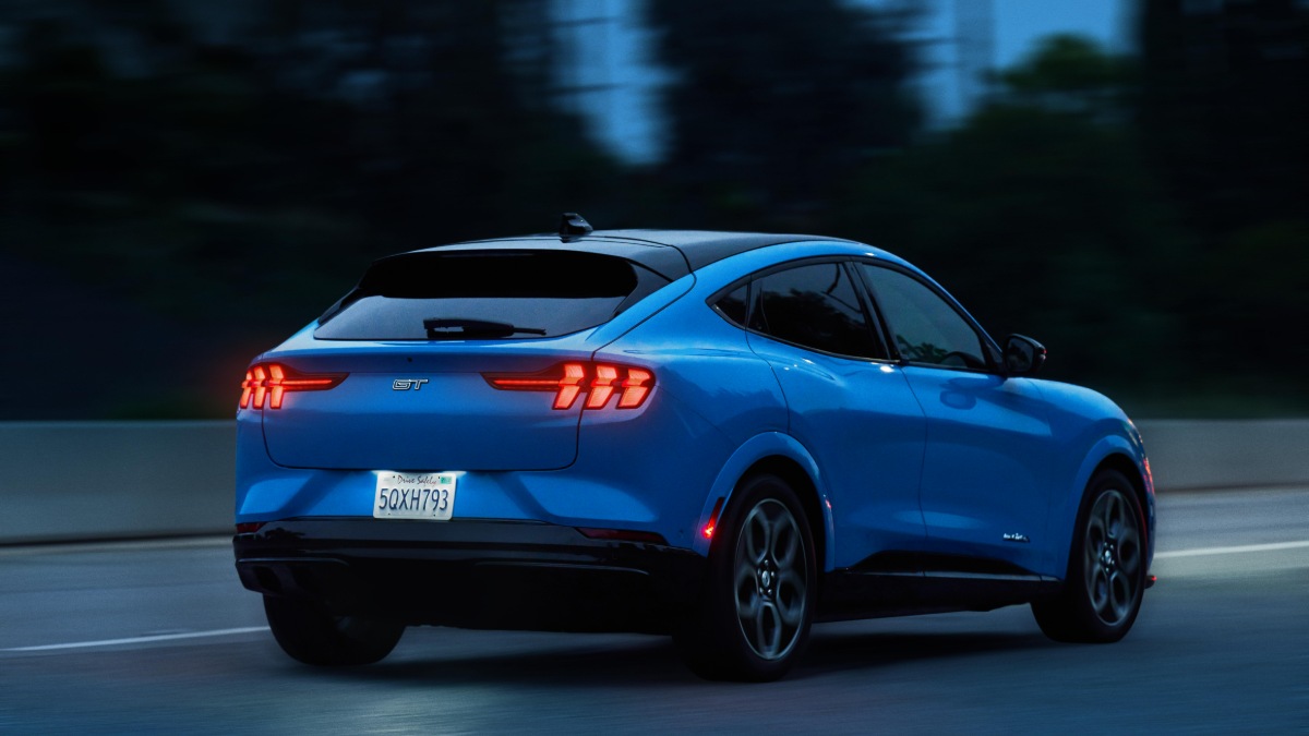 Blue Ford Mustang Mach-E GT driving at dusk with illuminated taillights on dark road