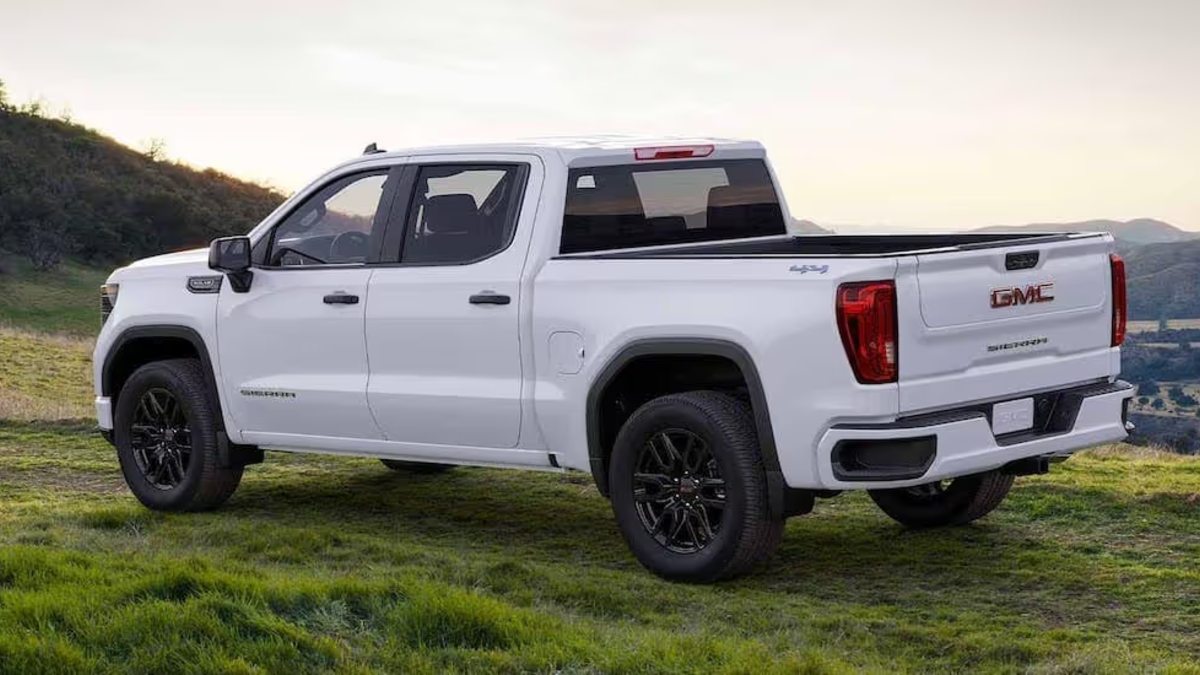 2023 GMC Sierra pickup in summit white, shown from rear three-quarter view on grassy hillside, featuring black wheels, LED taillights, and MultiPro tailgate.