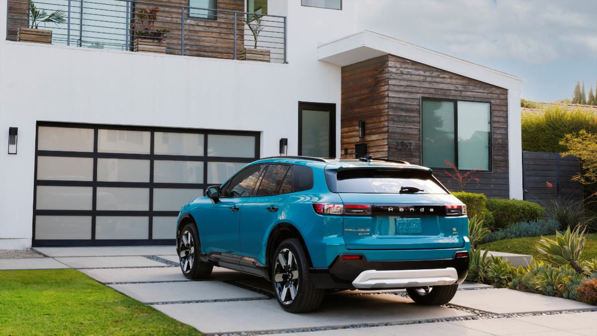 2024 Honda Prologue Elite in vibrant teal, rear three-quarter view, parked beside modern white house with wooden accents