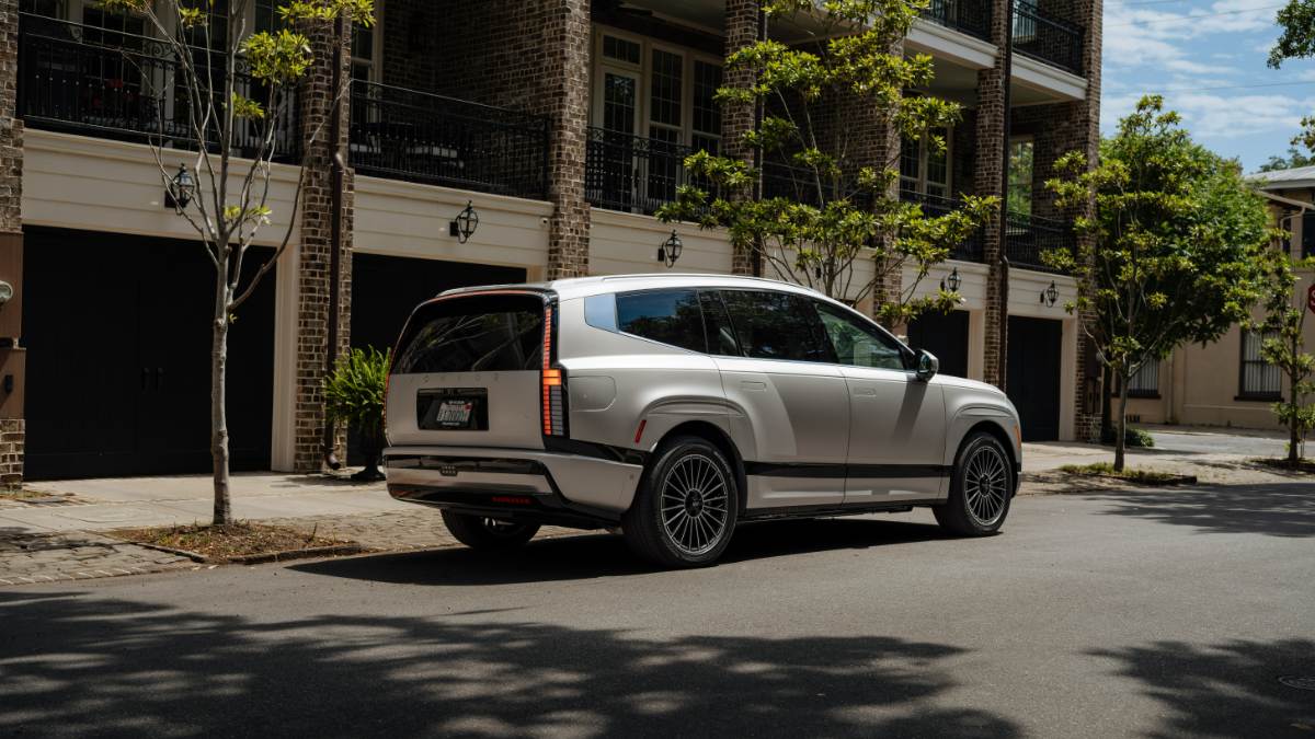 Hyundai Ioniq 9 in silver, rear three-quarter view, parked on urban street with brick buildings, featuring distinctive vertical taillights and black multi-spoke wheels.