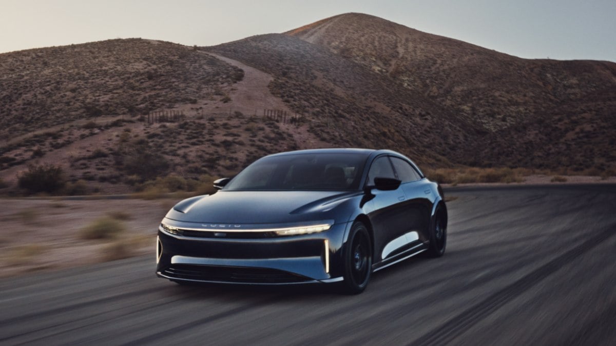 2024 Lucid Air in blue driving on desert highway, front three-quarter angle highlighting slim headlights and futuristic EV styling.