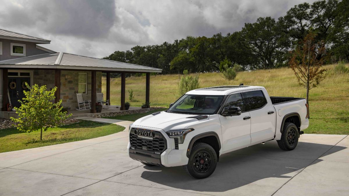 White Toyota Tundra pickup truck photographed from a front three-quarter angle parked in a residential driveway with countryside backdrop.