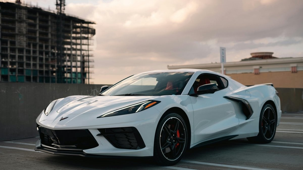 White Chevrolet Corvette C8 parked in a city parking structure with modern architecture in the background.