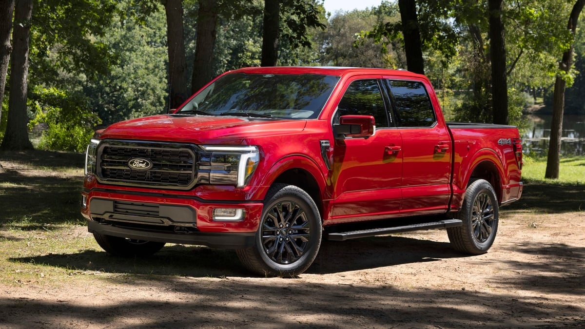 Red 2024 Ford F-150 Lariat parked near a wooded lakeside in a front three-quarter view.