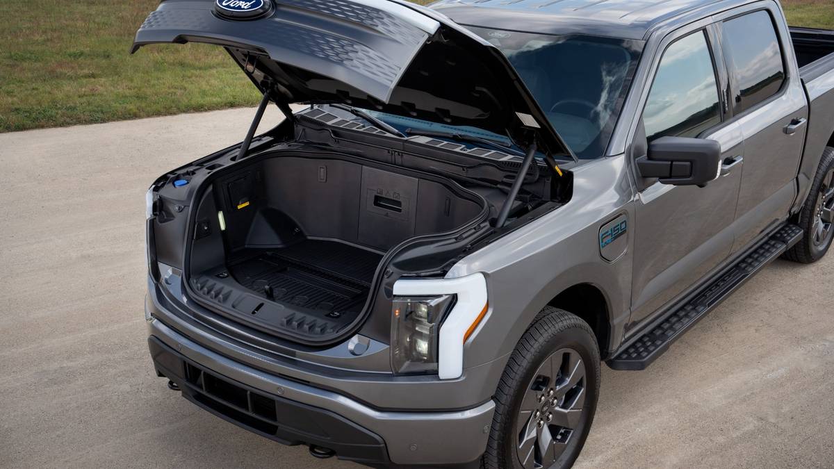 2024 Ford F-150 Lightning in gray with the front trunk (frunk) open, showing the large storage area and the Ford logo on the underside of the hood.