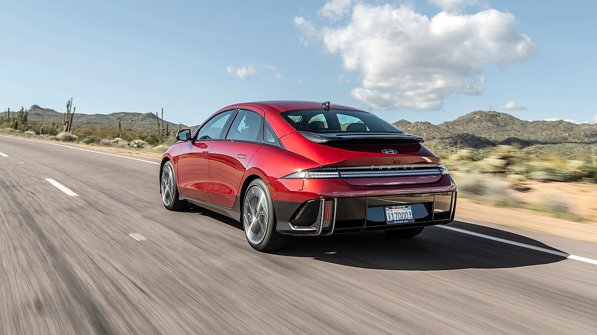 Red 2024 Hyundai Ioniq 6 Limited driving on a desert highway in a rear three-quarter action view.