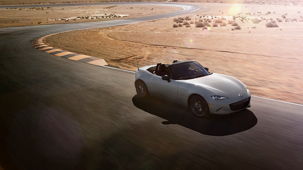 White 2024 Mazda MX-5 Miata convertible driving on a desert road course with the top down.