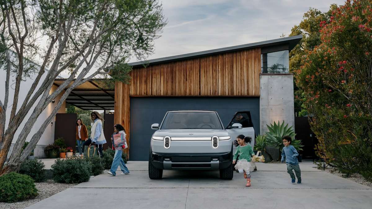 Gray Rivian R2 electric SUV parked in a modern home driveway as a family and children walk around the vehicle.