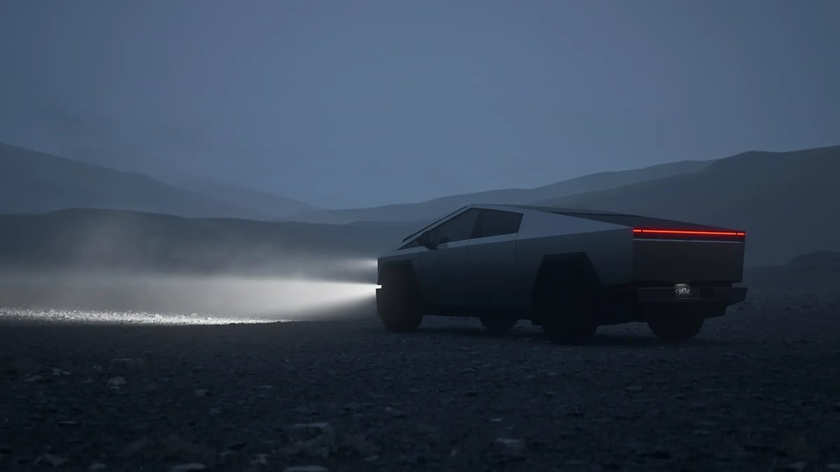 Tesla Cybertruck driving at night in a desert landscape with headlights on and rear light bar glowing.