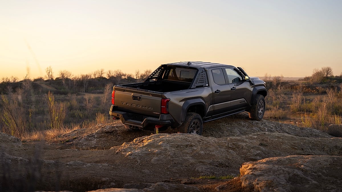 Bronze Oxide 2024 Toyota Tacoma Trailhunter shown from the rear on rocky off-road terrain at sunset.