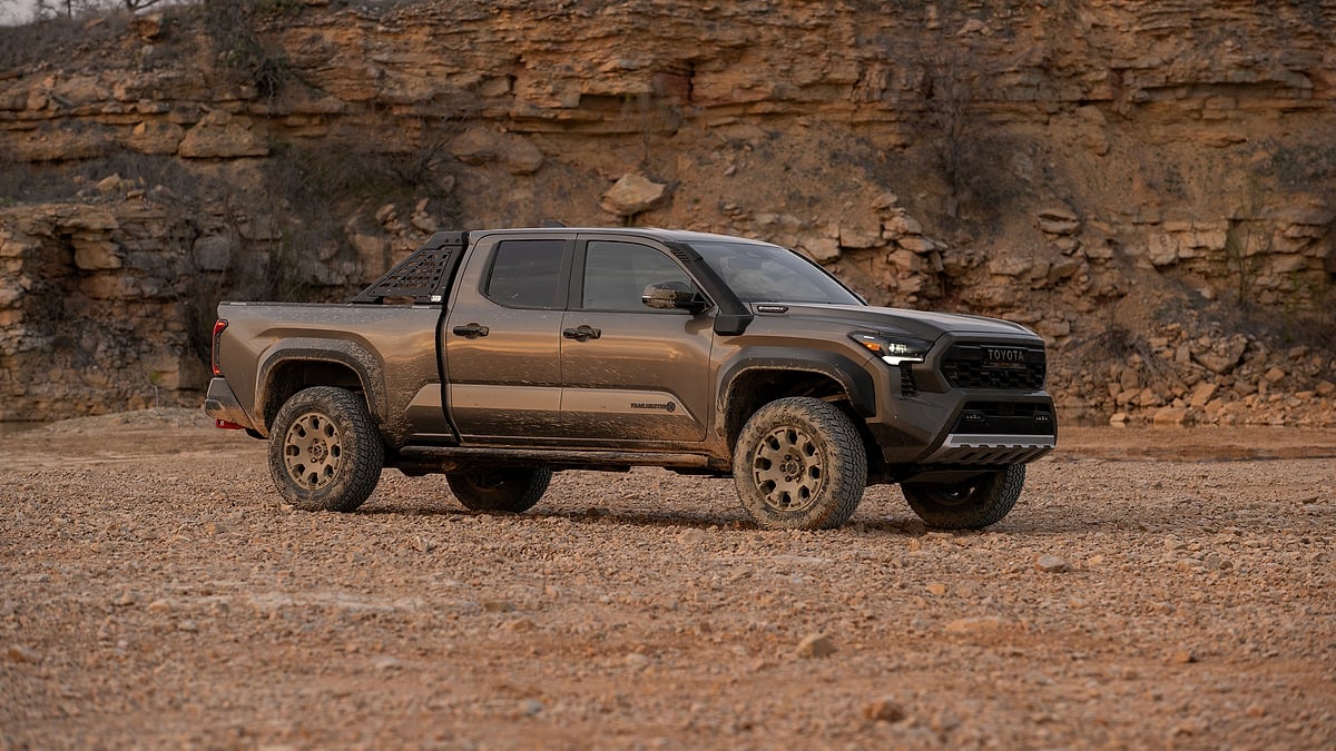 Bronze Oxide 2024 Toyota Tacoma Trailhunter parked on rocky terrain beside a layered stone cliff.