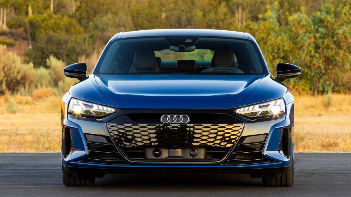 Blue Audi electric vehicle with illuminated LED headlights and large black honeycomb grille, outdoors.