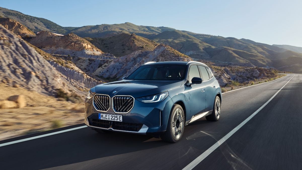 Blue BMW X3 SUV driving on mountain road with rugged rocky landscape and clear sky background
